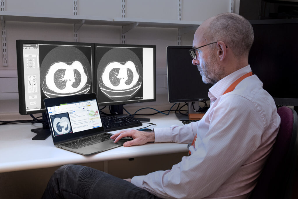 A man sits at a computer looking at CT scans.