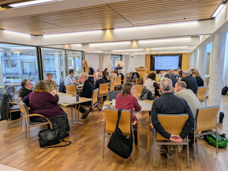 A group of people in a room sitting around tables having discussions.