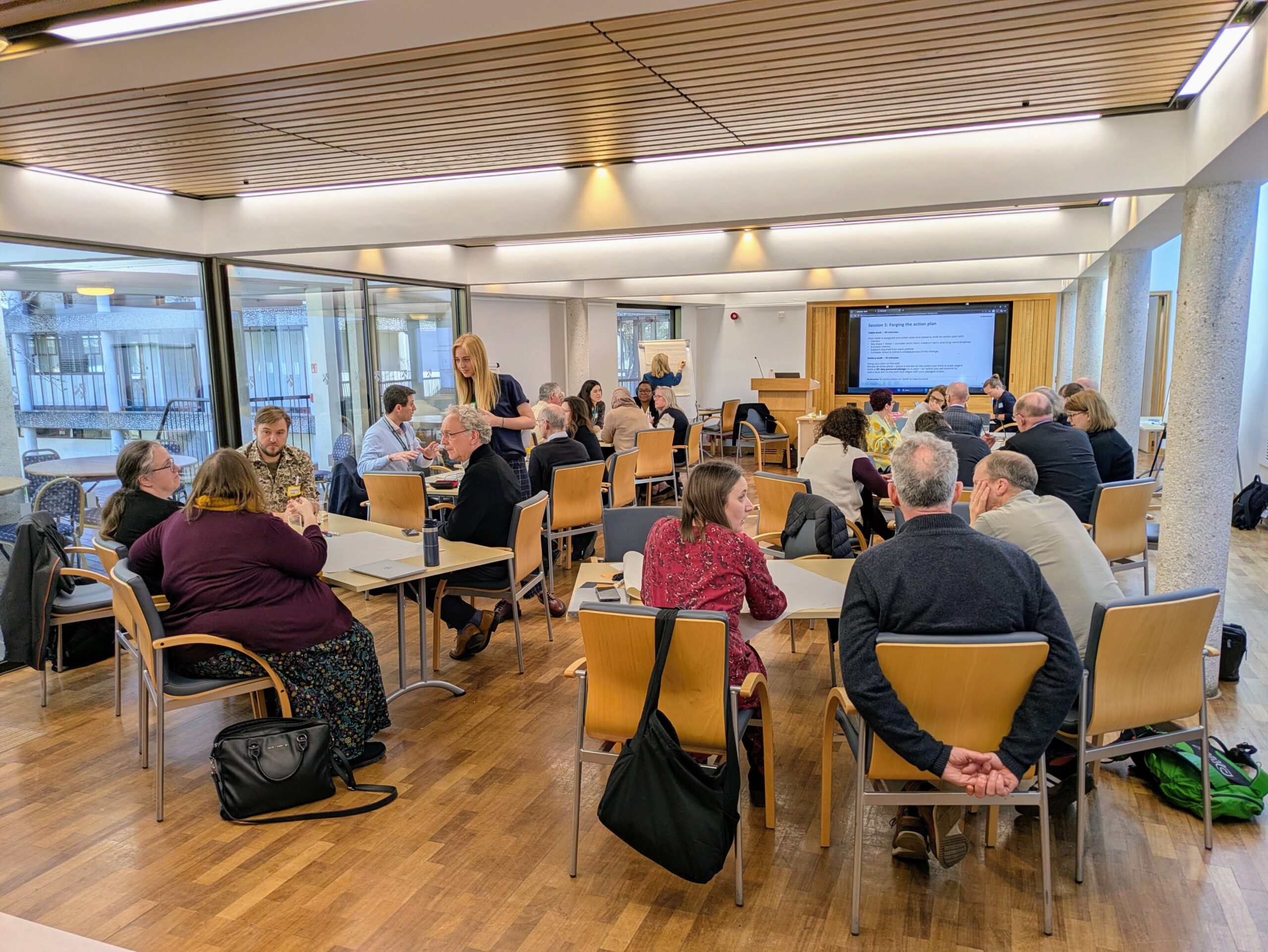 A group of people in a room sitting around tables having discussions.