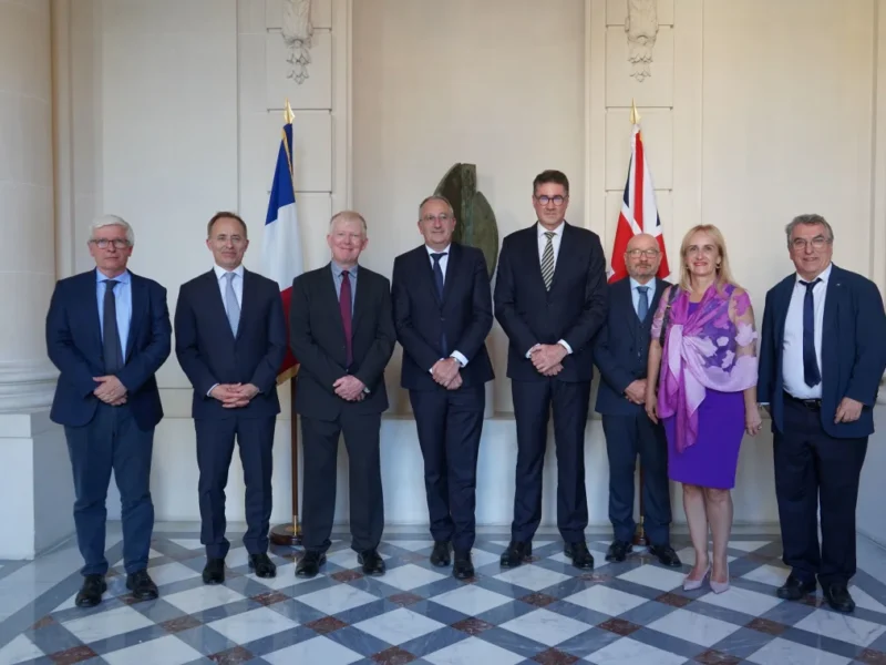 A group of people pose in front of UK and French national flags.