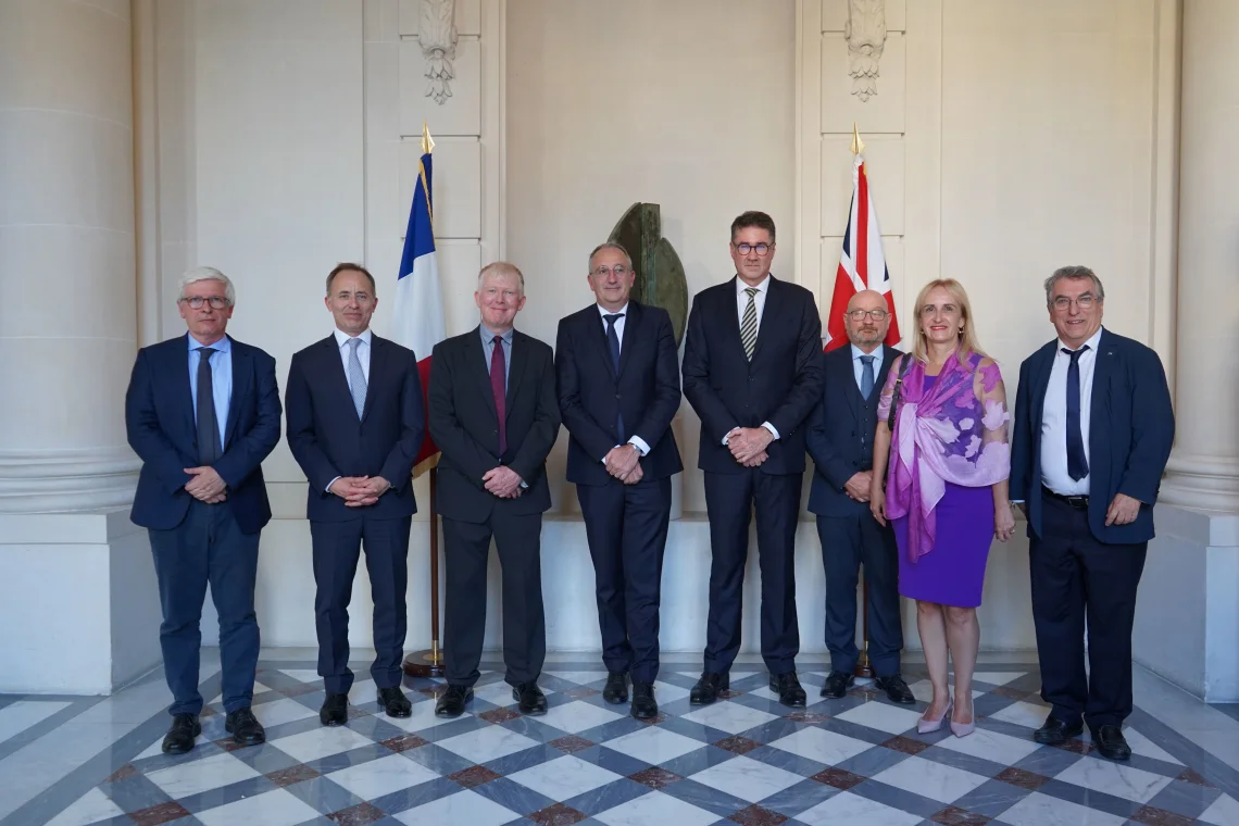 A group of people pose in front of UK and French national flags.