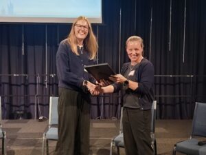 A woman is presented with an award in the form of a printed, framed certificate.