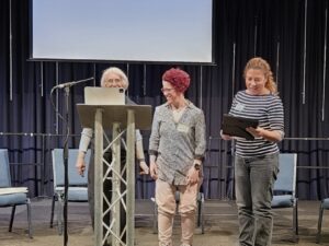 Three people stand on stage looking at a printed, framed certificate.