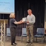 A man is given an award by a woman on stage