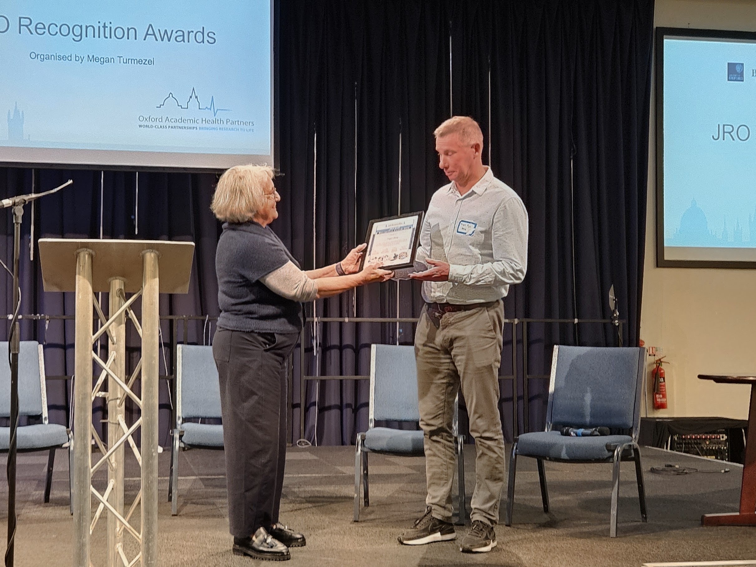 A man is given an award by a woman on stage
